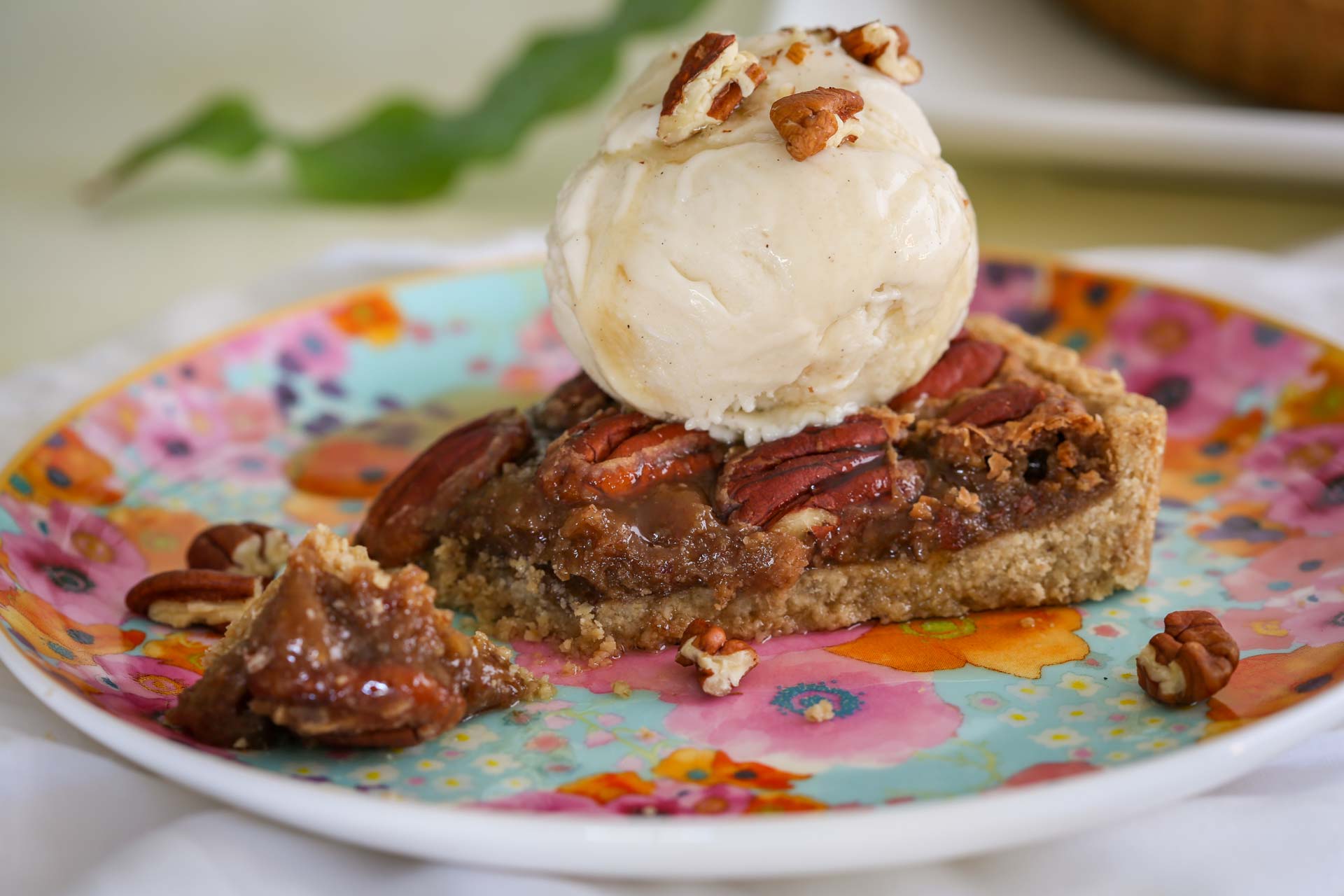A slice of ooey gooey maple pecan caramel pie topped with a smooth and decadent oat milk vanilla bean ice cream