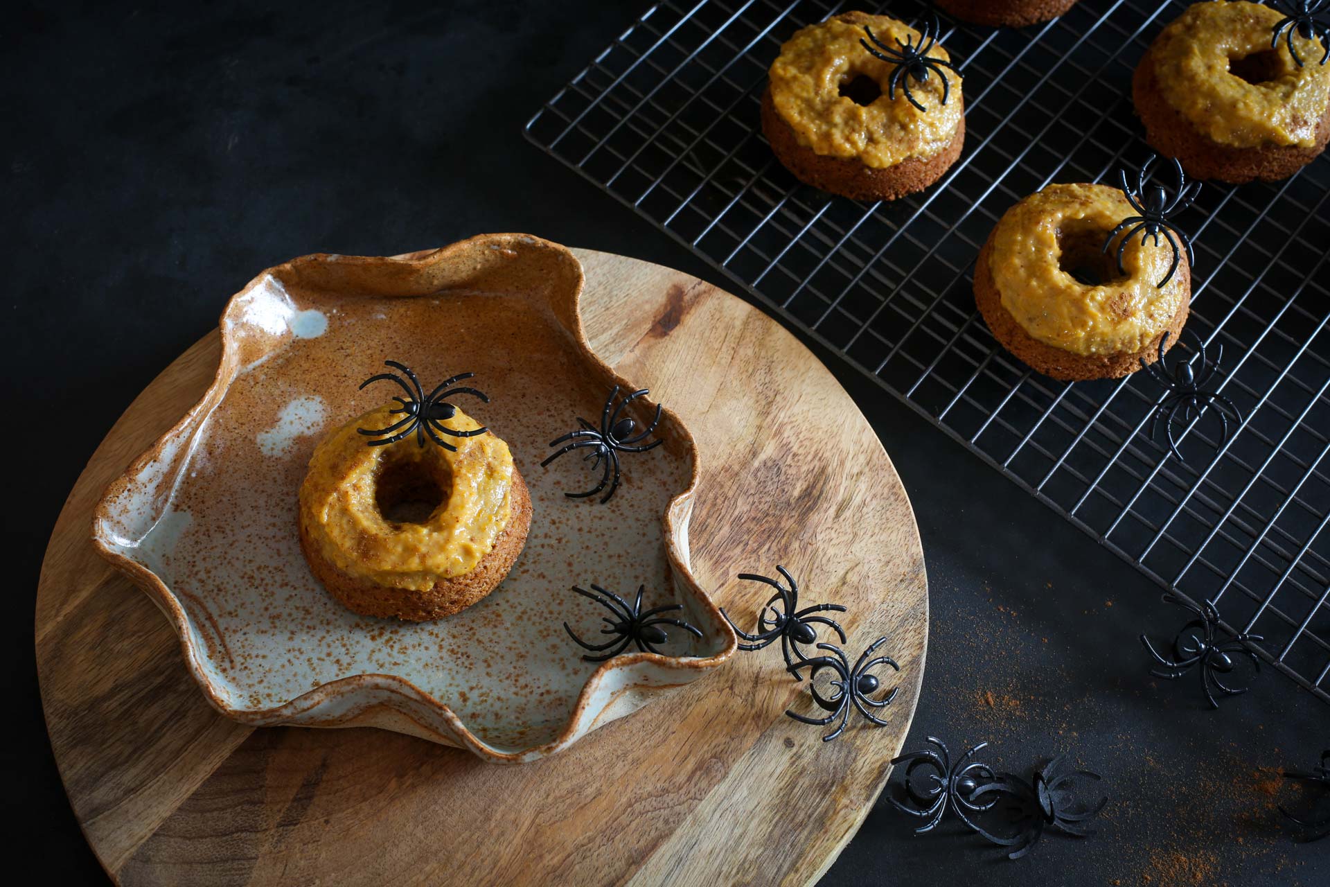 A pumpkin butter topped spiced pumpkin doughnut served on a wooden platter with spiders crawling for effect